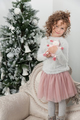 Child girl with sheep toy stand near Christmas tree