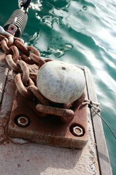 rusting metal mooring bollard for ships with chain and sea	