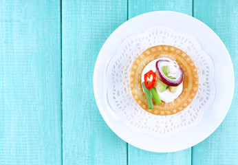 Tartlet with greens and vegetables with sauce on plate on table
