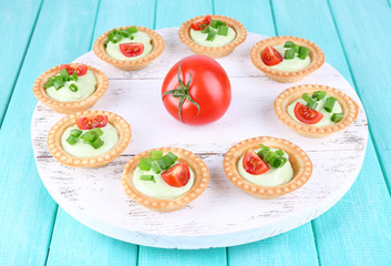 Tartlets with greens and vegetables with sauce on tray on table