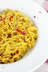 Spaghetti with pesto, chili flakes and chili on a white plate.