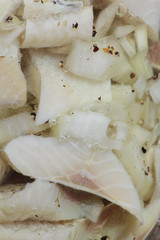 Closeup of a jar of herrings with chopped onion.
