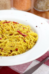 Spaghetti with pesto, chili flakes and chili on a white plate.