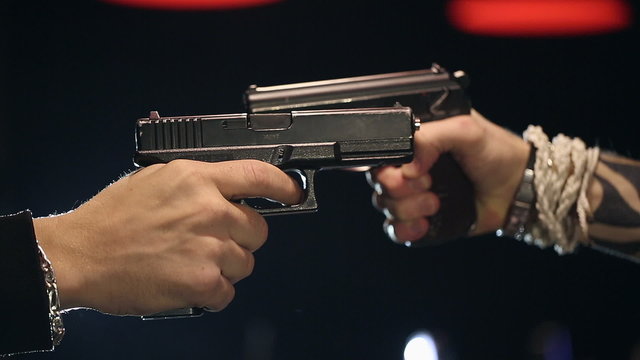 Two male hands with guns take aim at each other. Close up