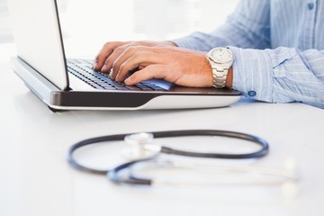 Man using laptop near a stethoscope on desk