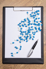 pills, clipboard and pen on wooden table