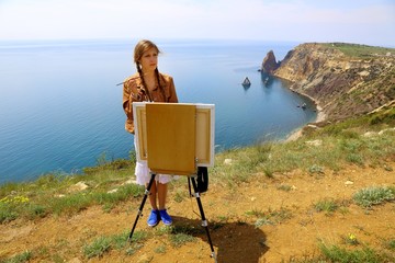 Fototapeta na wymiar girl artist draws on a mountain coast