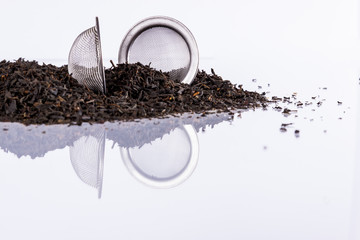 Black tea and tea strainer on white background.