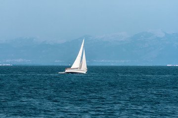 Fototapeta premium Sailboat floats quickly against the distant mountains