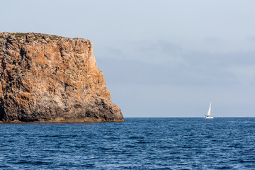 Fototapeta na wymiar View on a large rock and a sailboat at sea