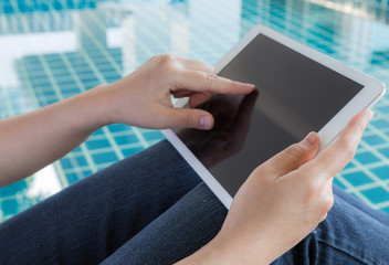 Woman working with tablet sitting at swimming pool