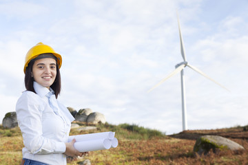 Female engineer holding blueprints at wind turbine site