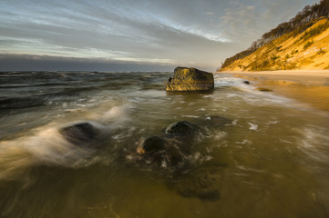 Kamienista plaża pod klifem  zalewana falami © Mike Mareen
