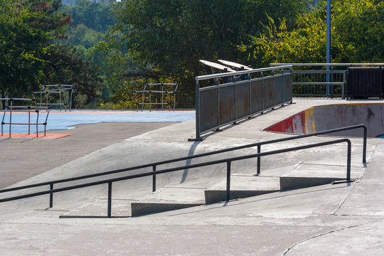 Empty skatepark at noon with ramps and grind rails.