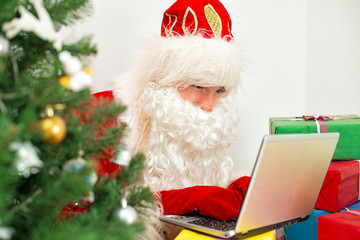 Santa Claus is using laptop at his workshop.