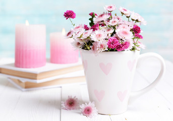 Beautiful flowers in cup on table on light blue background