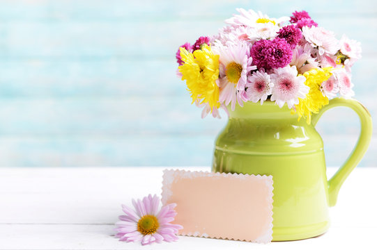 Fototapeta Beautiful flowers in pitcher on table on light blue background