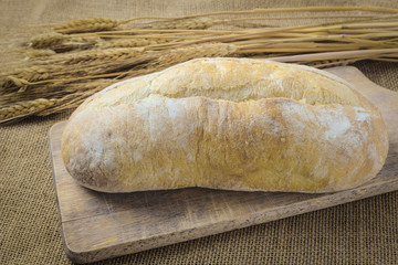 Bread on Bread Board with Wheat on Burlap Background
