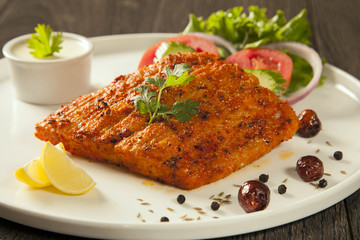 Grilled fish tikka served on a plate with salad and tarter sauce