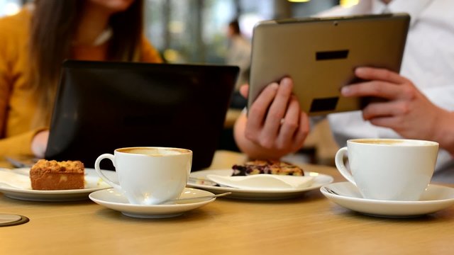 woman works on computer  and man works on tablet in cafe