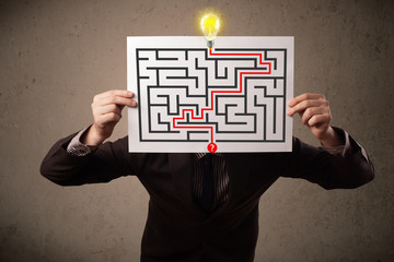 Businessman holding a paper with a labyrinth on it in front of h