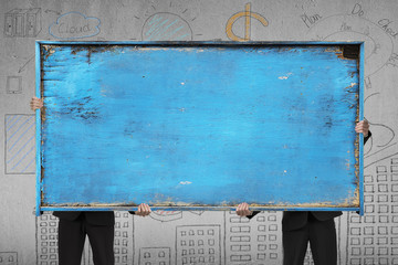 two businessman holding old blue blank wooden noticeboard