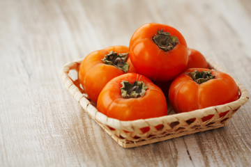 persimmon in a wicker basket on a light wooden background