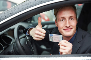 Young man holding drivers licence and thumps up