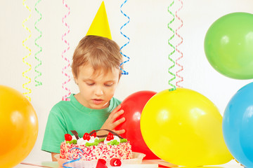 Fototapeta na wymiar Little boy in festive cap looking at the birthday cake
