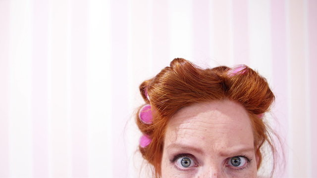 Young Redhead Woman Curlers In Hair Pulling A Face