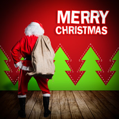 Weihnachtsmann steht vor Wand mit Merry Christmas Gruß