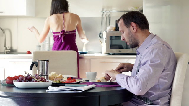 Man talking while his wife serving  him breakfast in the kitchen