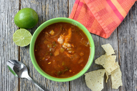 Tortilla Soup with Chips, fresh lime and spoon on Rustic Wood Ba