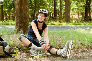 Young woman on roller skates sitting holding foot