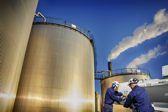 oil gas and workers with large industrial storage tanks