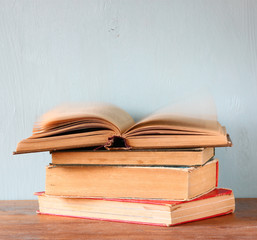 stack of old books over wooden shelf. the book at the top is ope