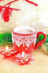 Cup of hot cocao with red poinsettia candle and pine
