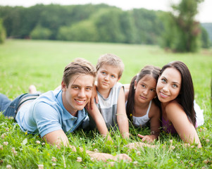 Junge glückliche Familie liegt im Sommer im Gras