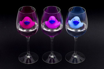 Pink, purple and blue rubber ducks in wineglasses