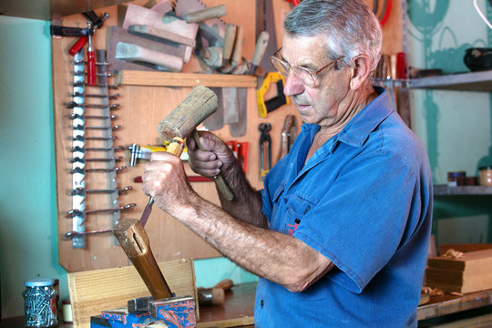 man working carving wood with a chisel and hammer