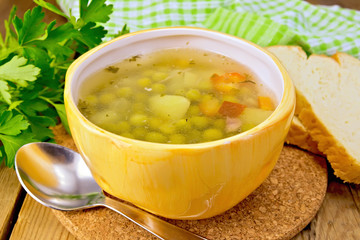 Soup of green peas in yellow bowl with bread on board