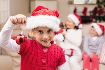 Cute little girl wearing santa hat holding bauble