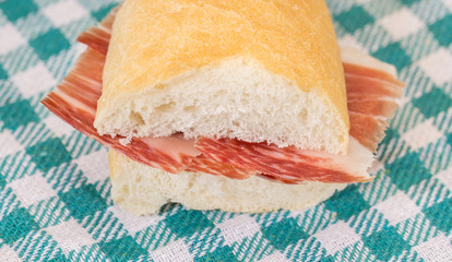 Front view of Serrano ham sandwich over checkered tablecloth