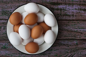 Chicken eggs in a glass and a metall dish on the purple boards