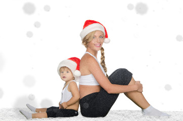 woman with child sitting on snow in Santa hats