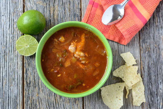 Tortilla Soup with Chips, fresh lime and spoon on Rustic Wood Ba