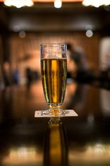 Glass of beer illuminated by the bar lighting.