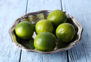 Fresh juicy limes on plate on wooden background