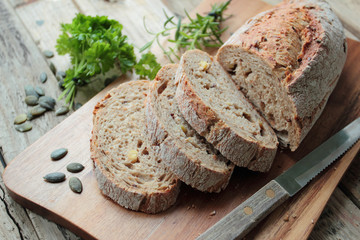 Crunchy wholemeal bread with knife on wooden cutting board