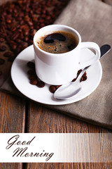Cup of coffee and coffee beans on napkin on wooden background